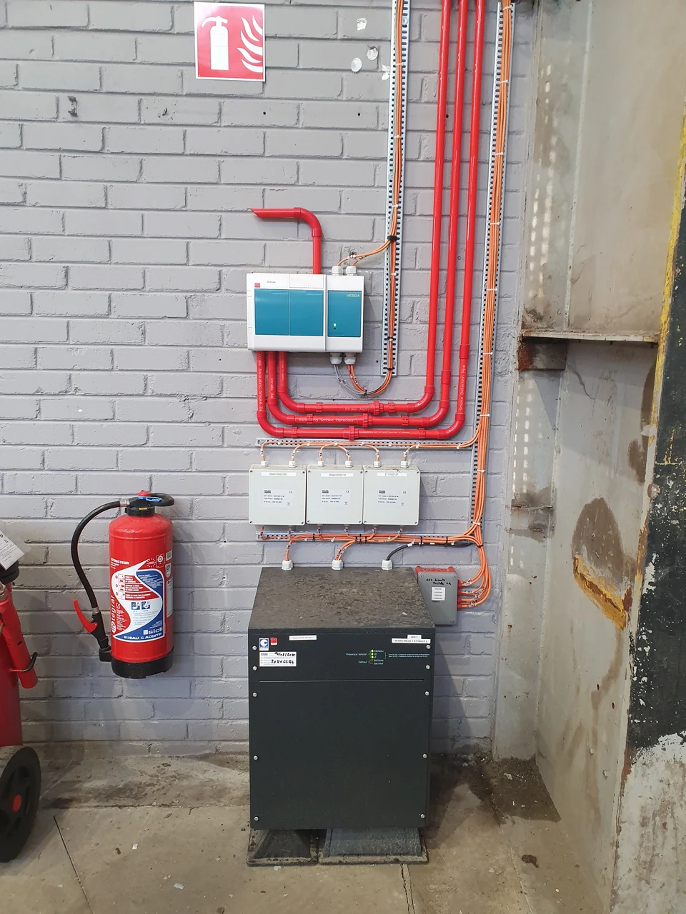 Ensemble de détection incendie avec détecteur VESDA, interfaces, coffret et extincteur dans un bâtiment industriel